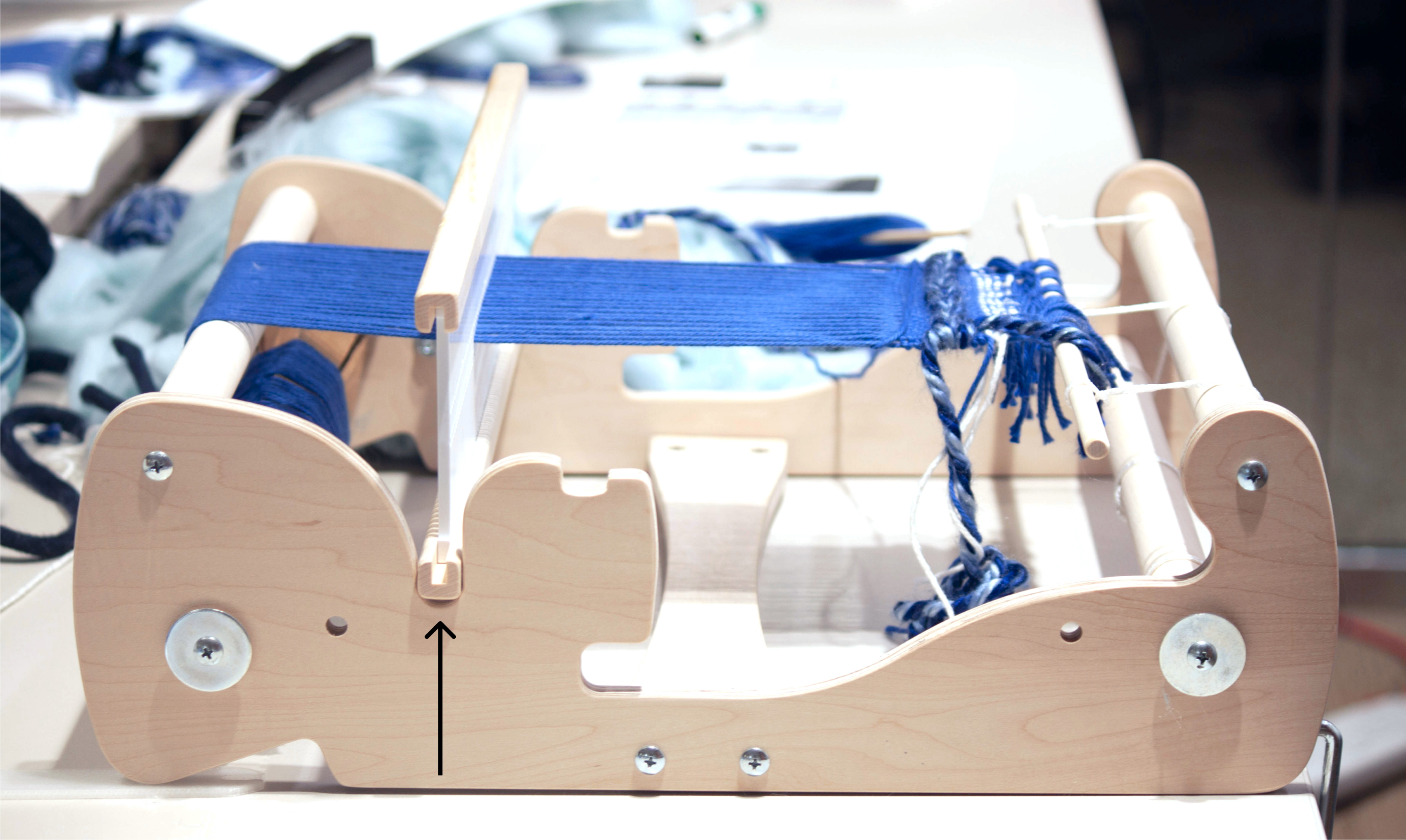 Wooden loom sitting on table with blue thread strung taught.