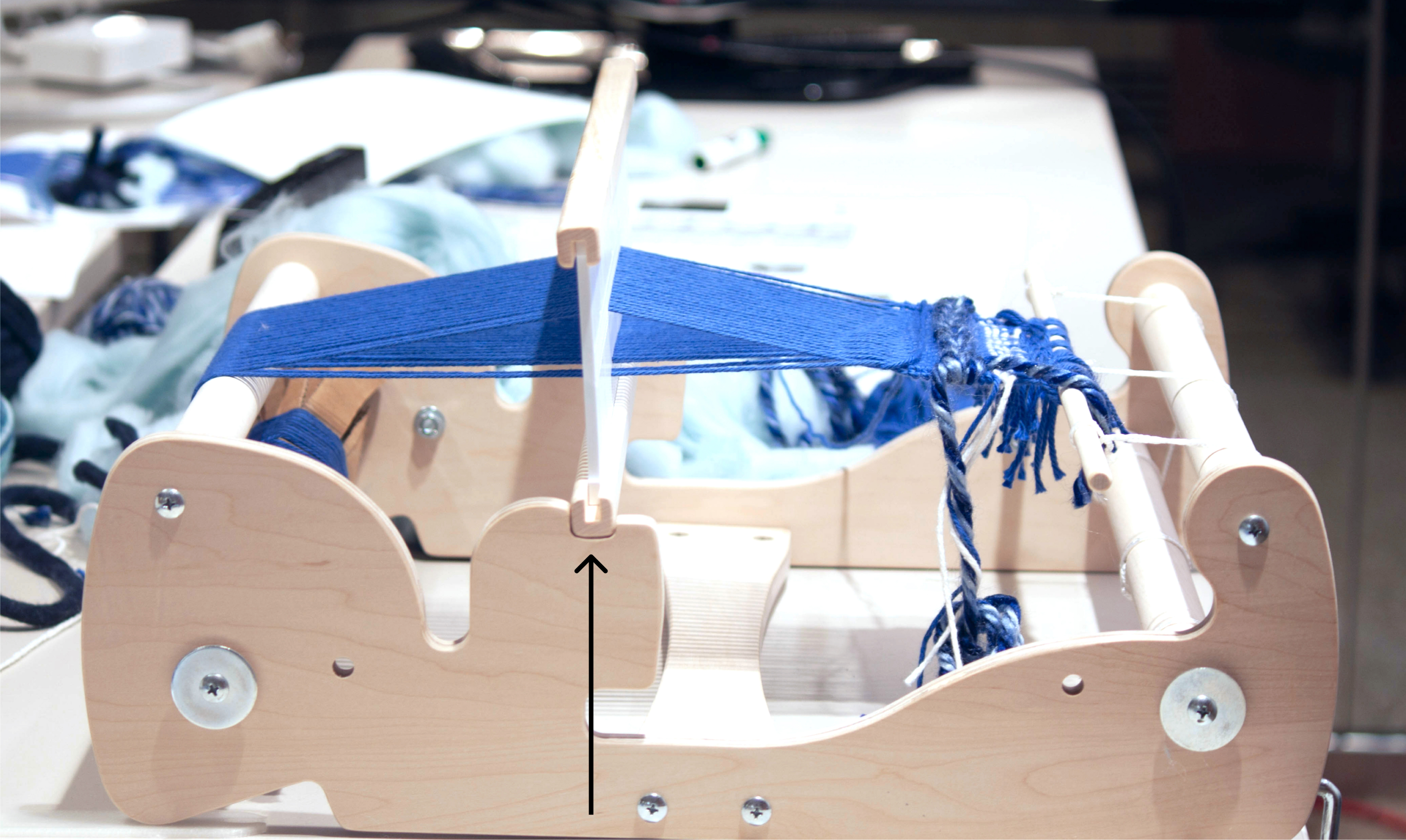 Wooden loom sitting on table with blue thread strung taught, pulled upwards.