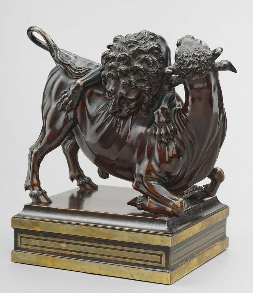 Bronze statue, deep brown color, of a lion biting into the side of a bull, who turns its head to face the lion.